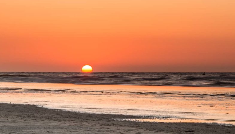 Het strand bij Paal 9 op Texel ligt verlaten bij zonsondergang.